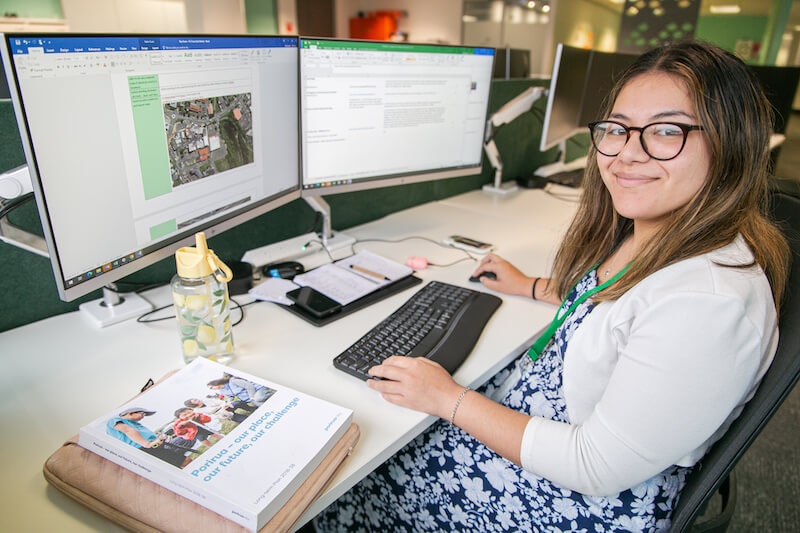 About Partners Porirua. Woman sitting at her desk smiling.